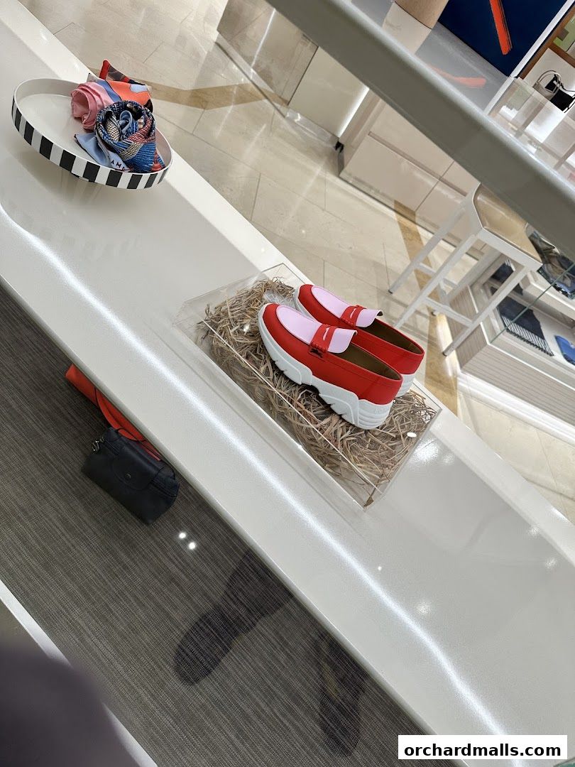 A display of stylish red and pink loafers and folded scarves inside a modern retail store.