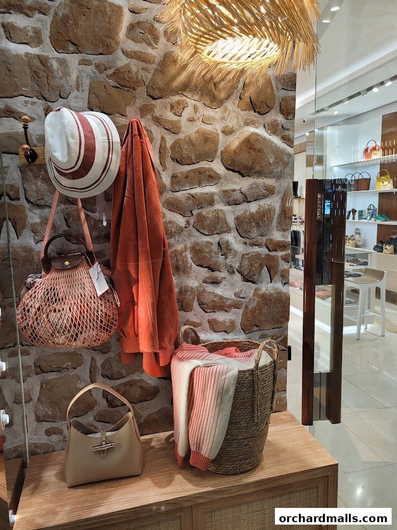 A display of Longchamp handbags, a hat, and clothing against a stone wall.