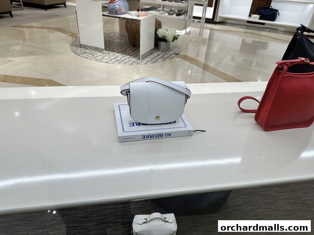 A display of stylish Longchamp handbags in various colors on a white counter.