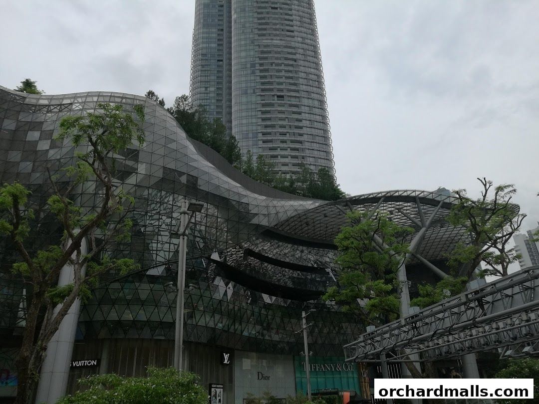 Exterior view of a modern shopping mall with iconic brand storefronts and skyscrapers.