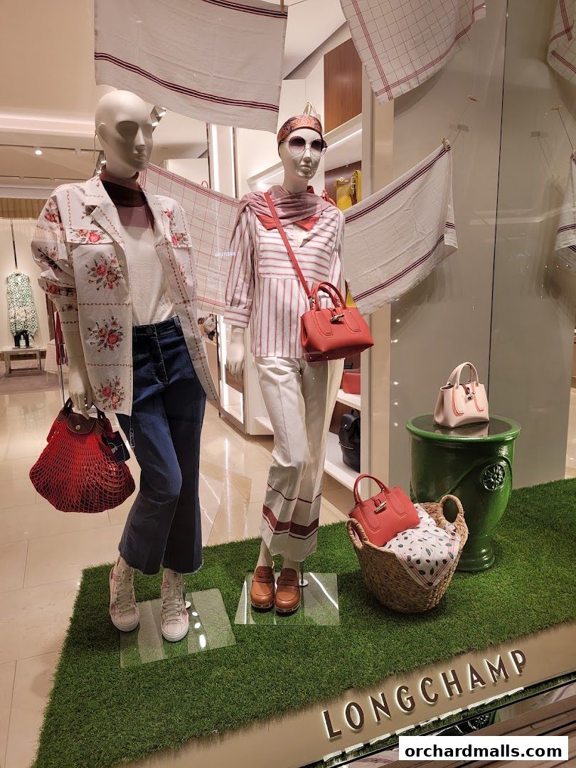 Two mannequins display Longchamp fashion with handbags and accessories in a store window.