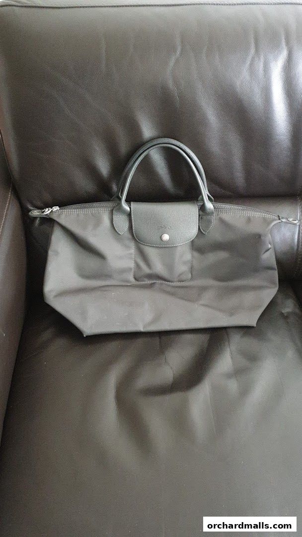 A dark grey Longchamp handbag rests on a brown leather couch.