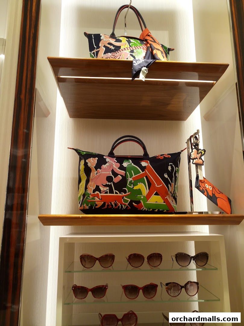A display of Longchamp handbags and sunglasses on shelves in a well-lit store.