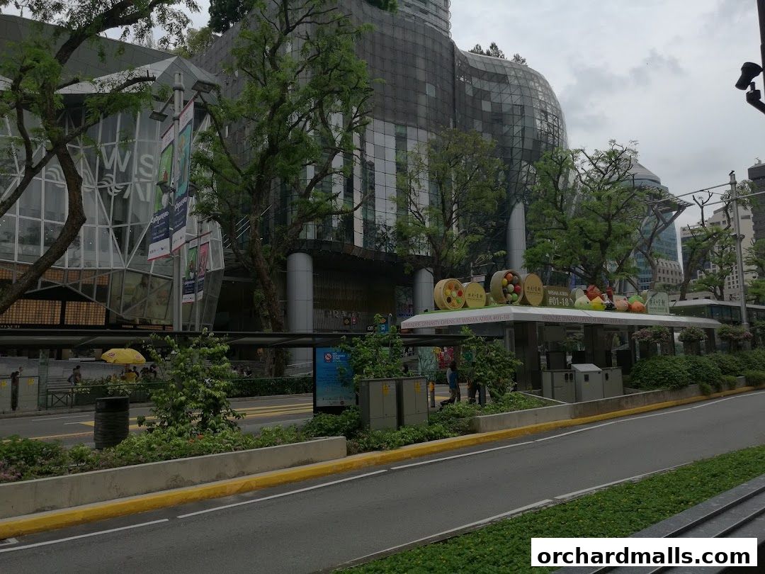 A street view of a modern building with trees and a bus stop shelter.