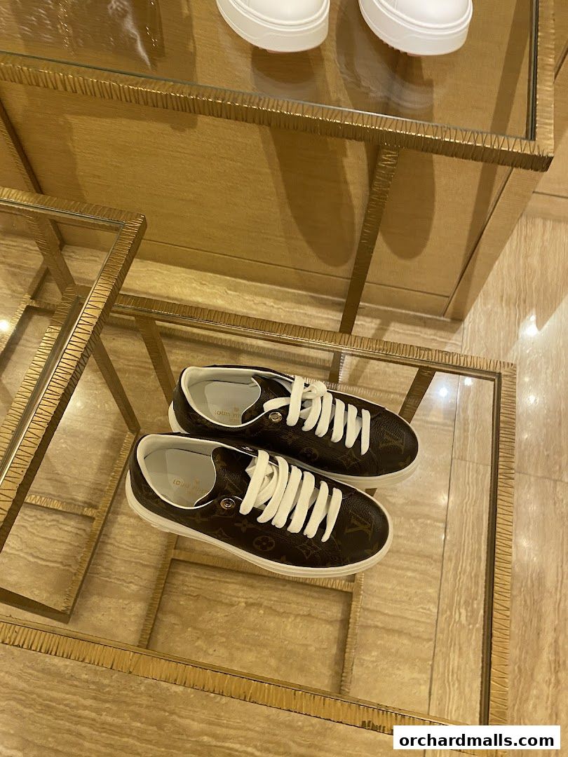 A pair of Louis Vuitton monogram sneakers displayed on a glass shelf.