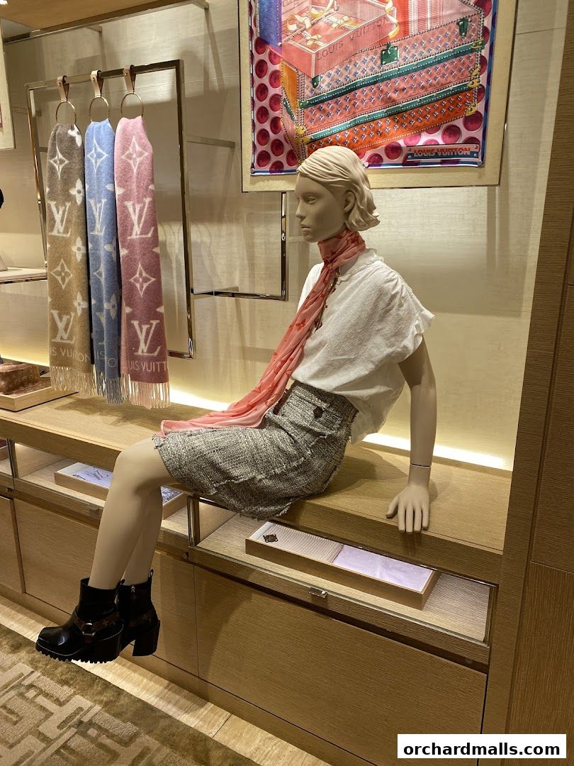 Mannequin displays Louis Vuitton scarves, skirt, and boots in a luxury retail setting.