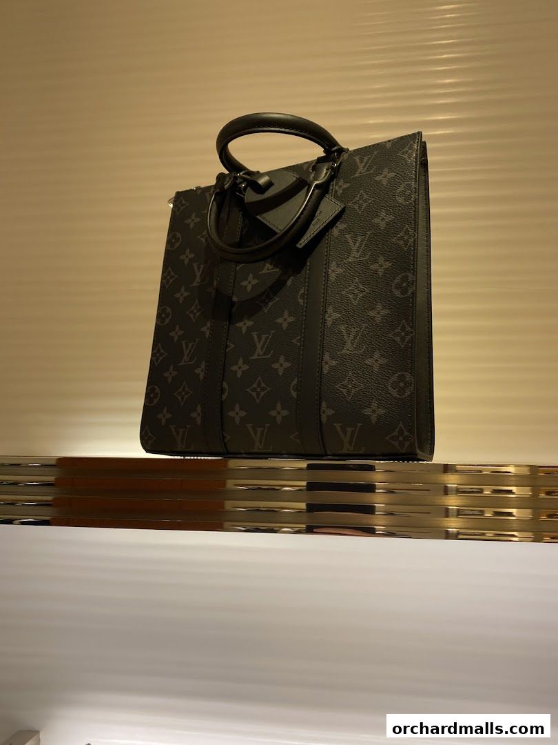 A Louis Vuitton monogrammed tote bag displayed on a shelf with warm lighting.