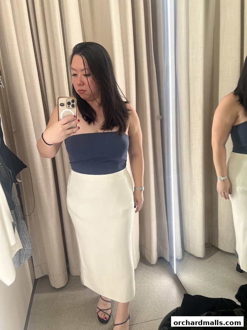 A woman tries on a navy blue strapless top and a cream-colored midi skirt in a fitting room.