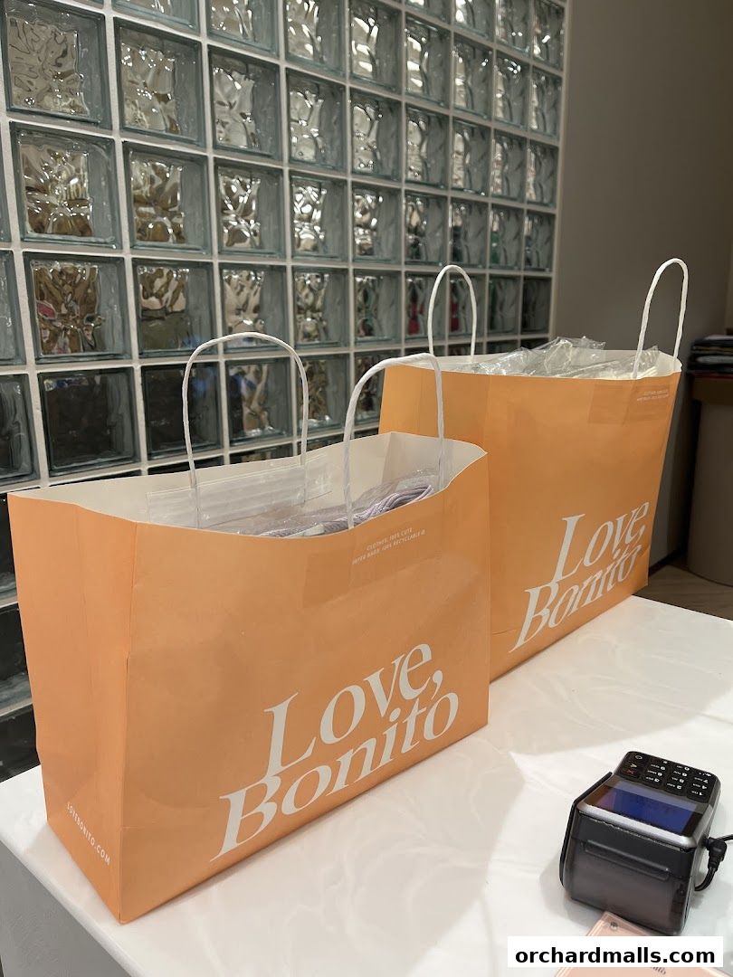 Two orange shopping bags with the 'Love, Bonito' logo are placed on a white surface.