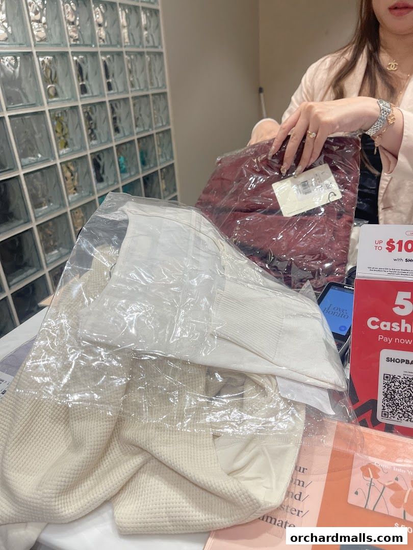 A person is holding packaged clothing items from Love, Bonito at a counter.