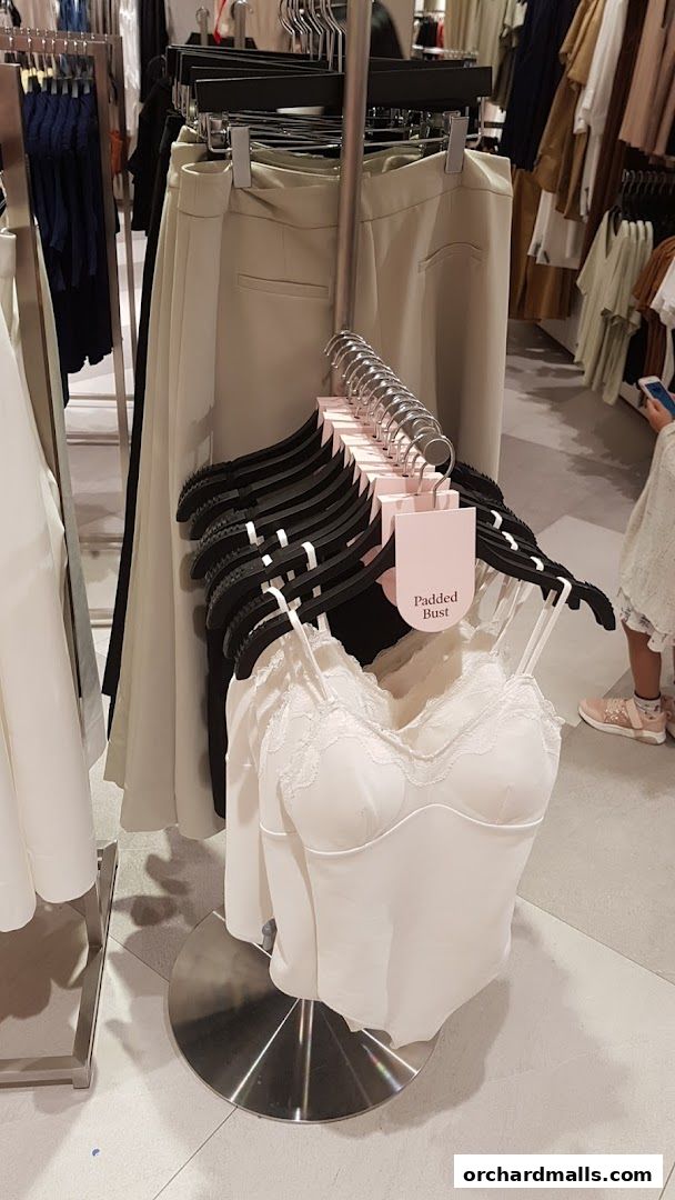 A display of white camisoles with lace trim and beige trousers in a clothing store.