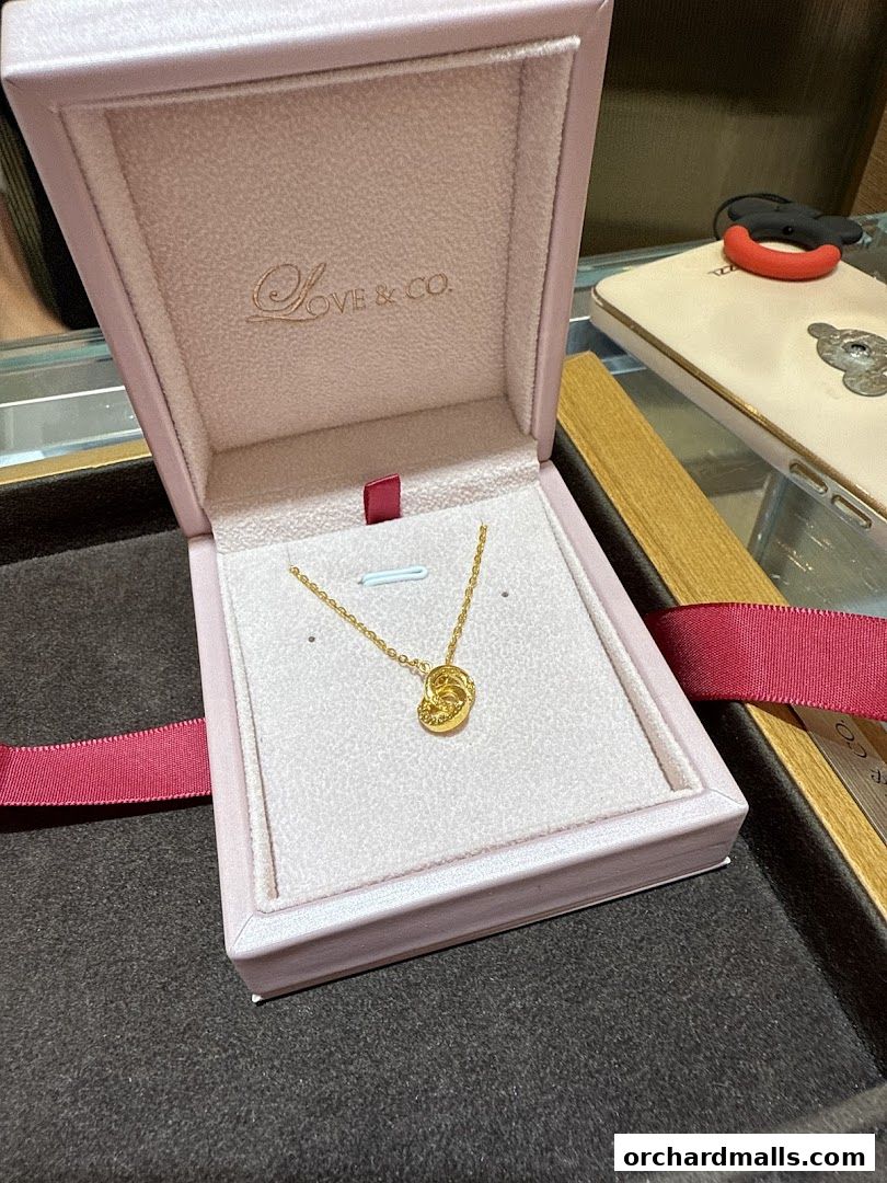 A gold necklace with a knot pendant in a pink jewelry box.