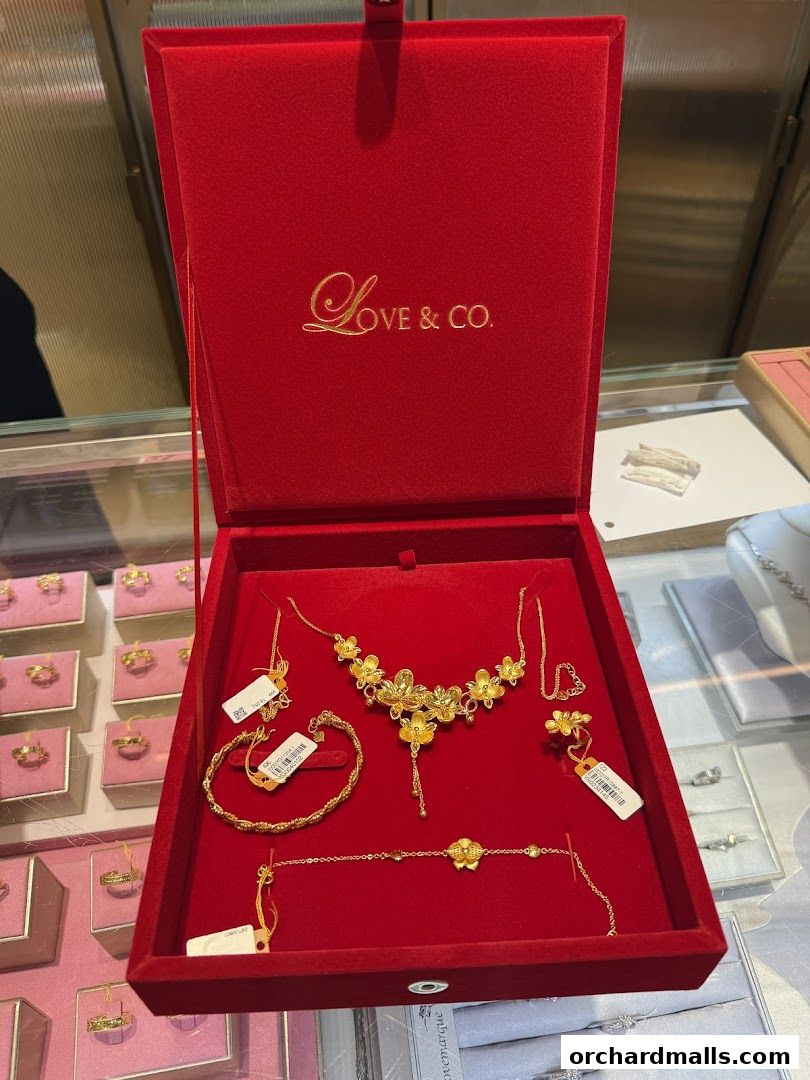 A red velvet jewelry box displaying a gold floral necklace, bracelet, and earrings.