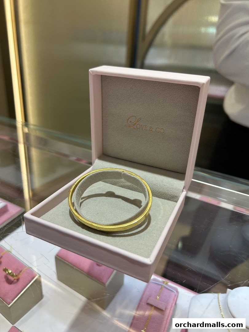 A gold bangle is displayed in an open pink jewelry box.
