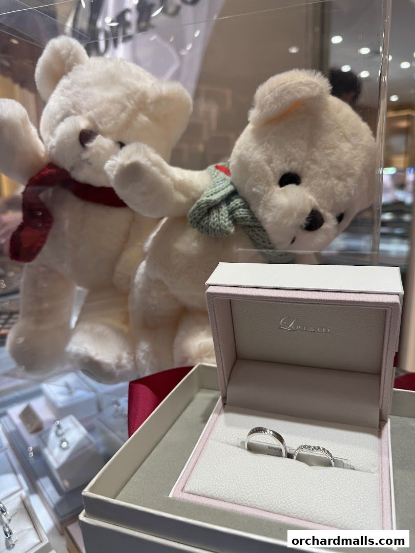 Two teddy bears and a ring box with wedding bands are displayed in a jewelry store.