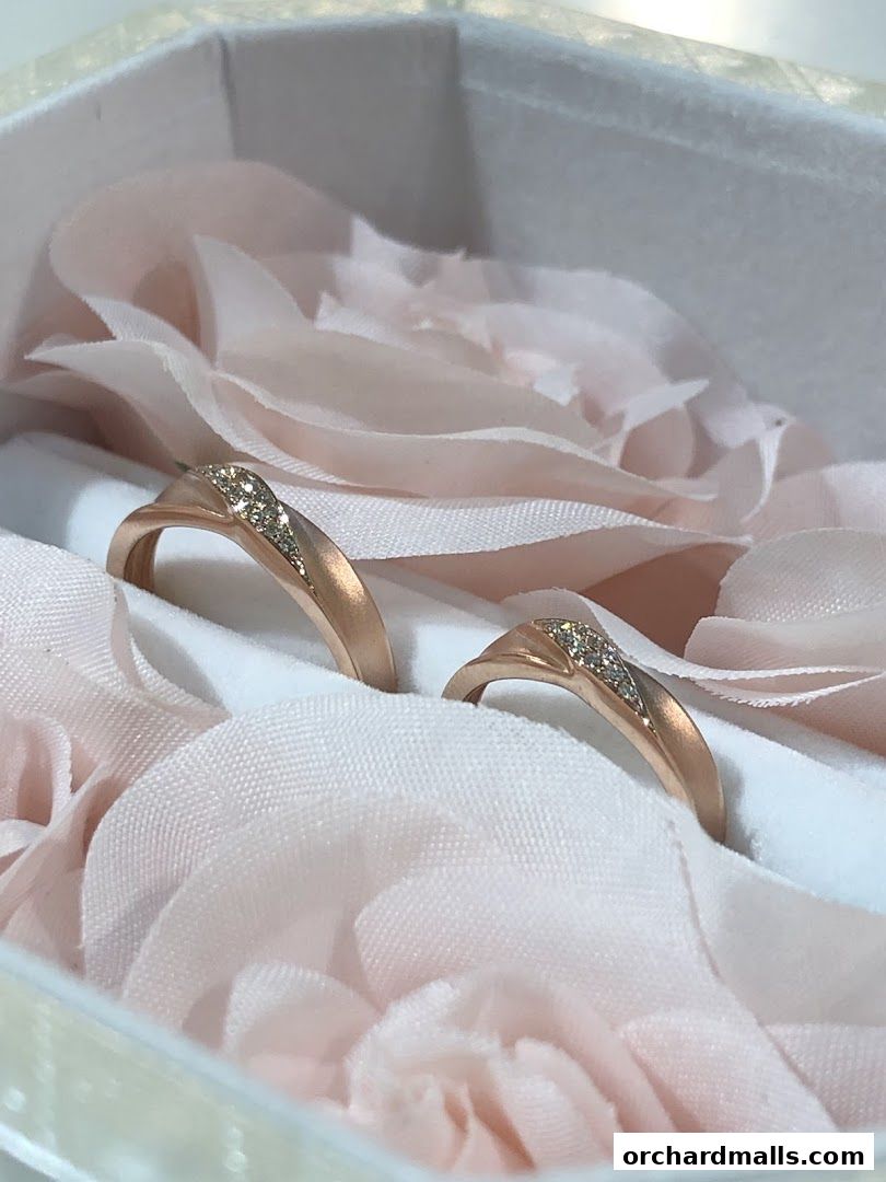 Two rose gold wedding bands with diamonds nestled in soft pink fabric.