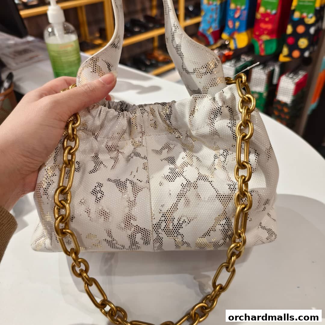 A hand holds a stylish white handbag with a gold chain and a unique speckled pattern.