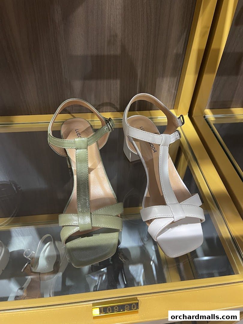 Two stylish sandals, one olive green and one white, displayed on a shelf.