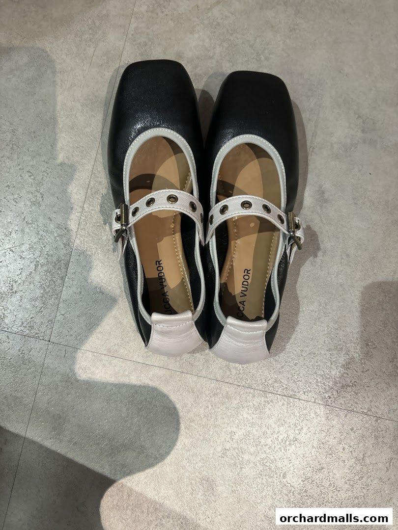 A pair of black and white square-toe ballet flats with buckle straps.