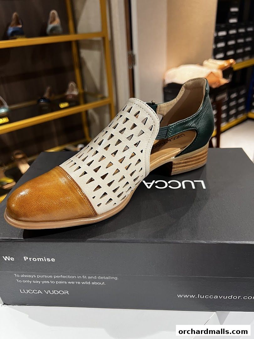 A stylish two-tone sandal with cut-out details rests on its branded box.