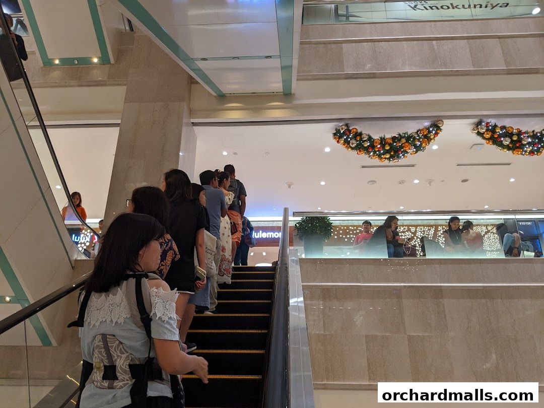 People queuing on an escalator in a mall, with a lululemon store visible.