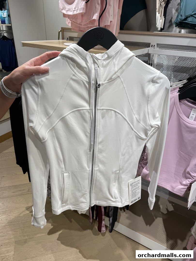 A person holds a white lululemon hooded jacket with a zipper and pockets.