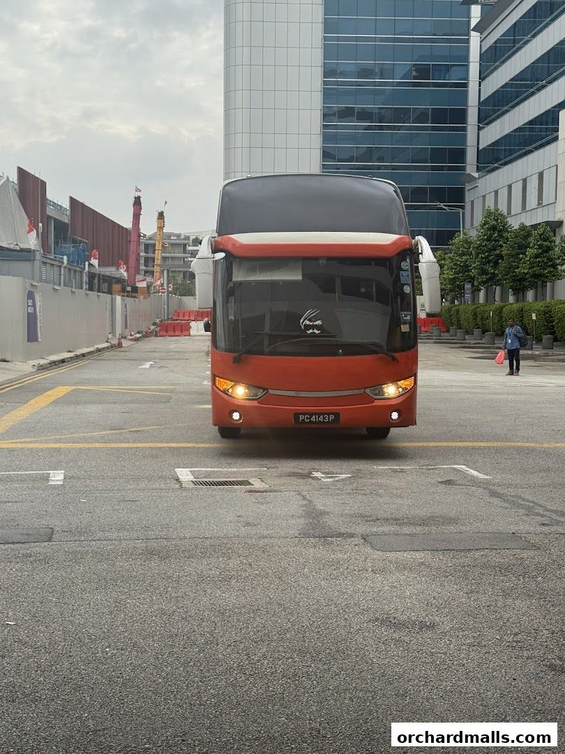 A bright orange double-decker bus is parked on a street with modern buildings in the background.