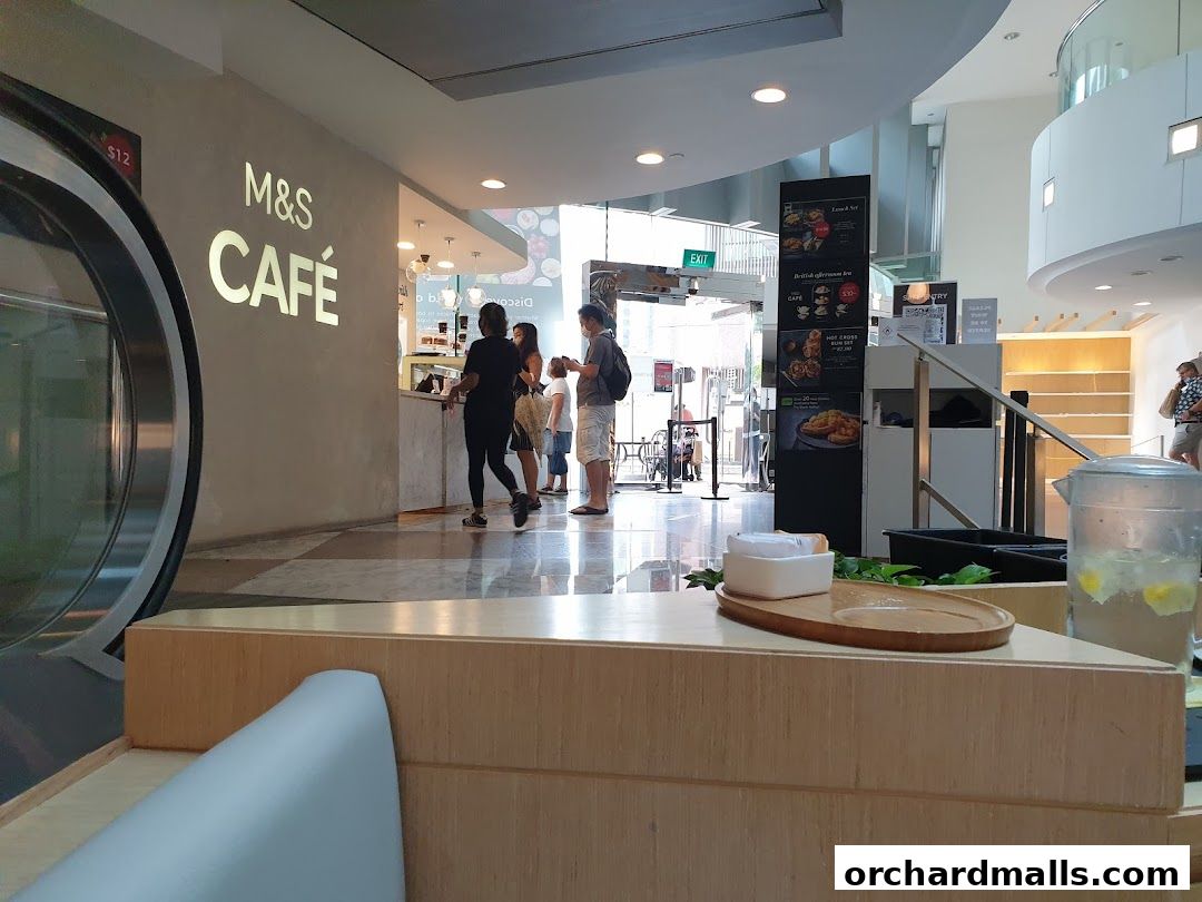 Interior view of M&S Cafe with customers ordering at the counter and a display of menu boards.