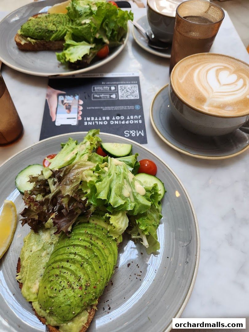 Two plates of avocado toast with salad and two coffees on a marble table.