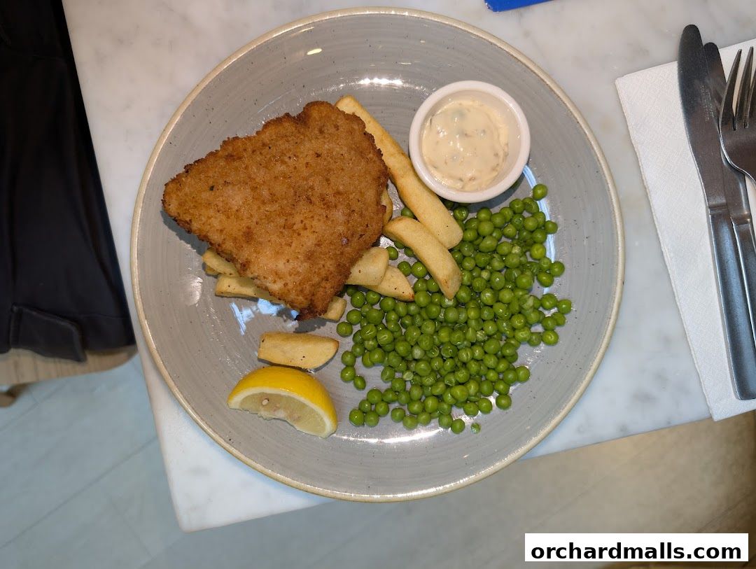A plate of fish and chips with peas, lemon, and tartar sauce.