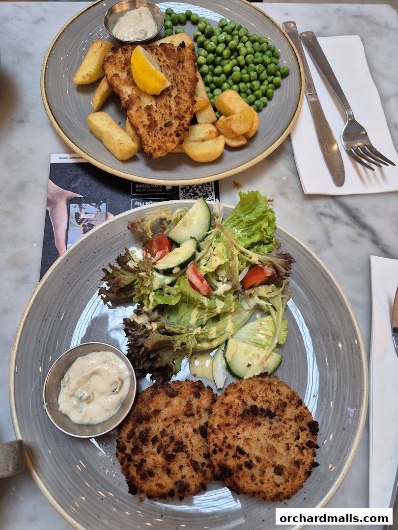 Two plates of food, one with fish and chips, the other with patties and salad.