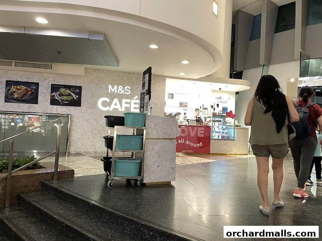 The entrance to M&S CAFE with a counter, display cases, and people walking by.