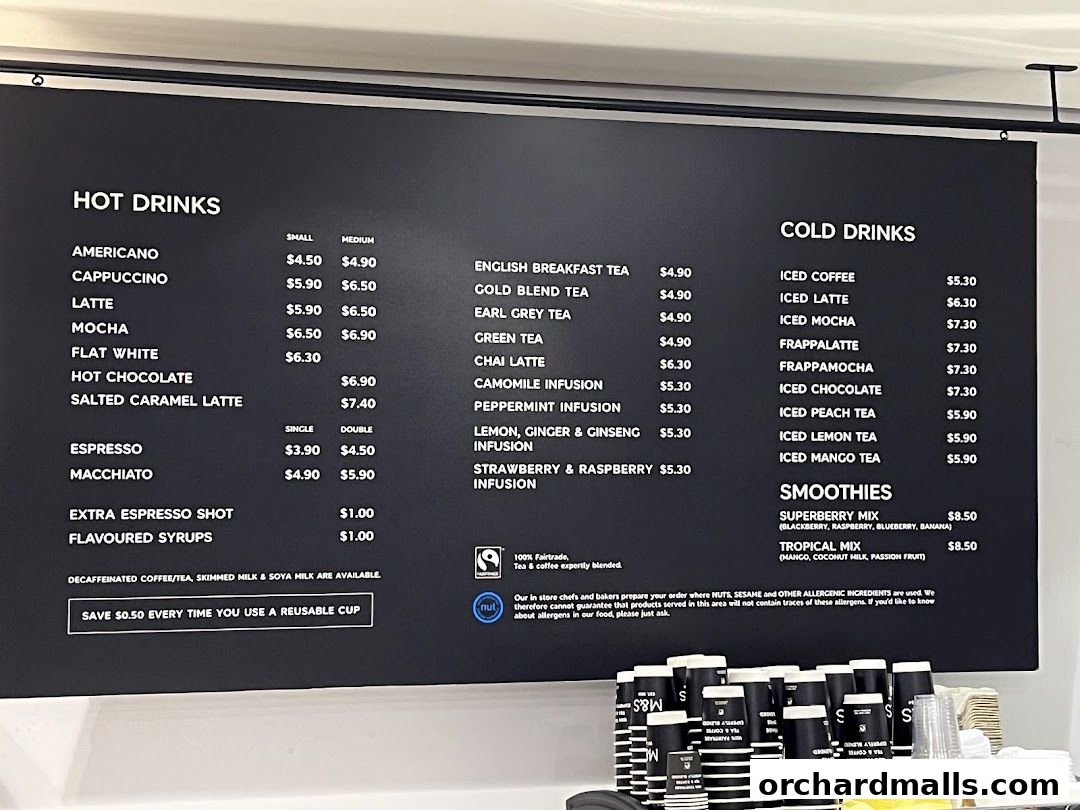 A black menu board displays hot drinks, cold drinks, and smoothies with prices.