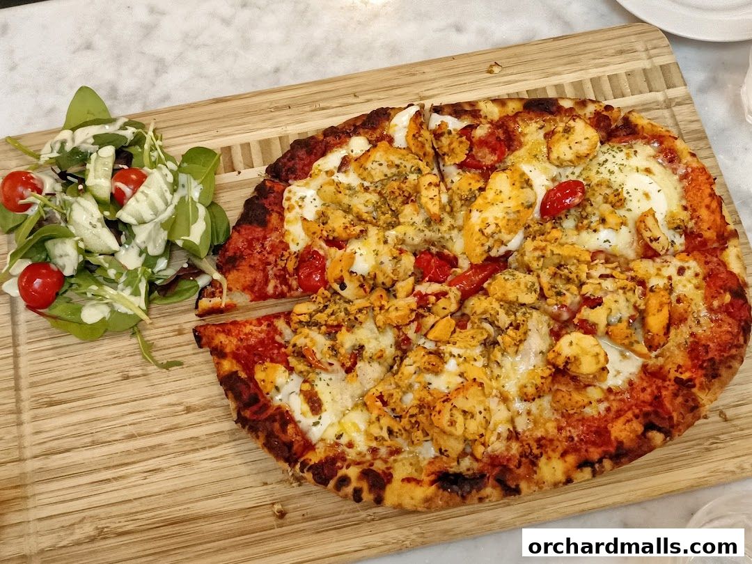 A delicious chicken pizza with a side salad served on a wooden board.