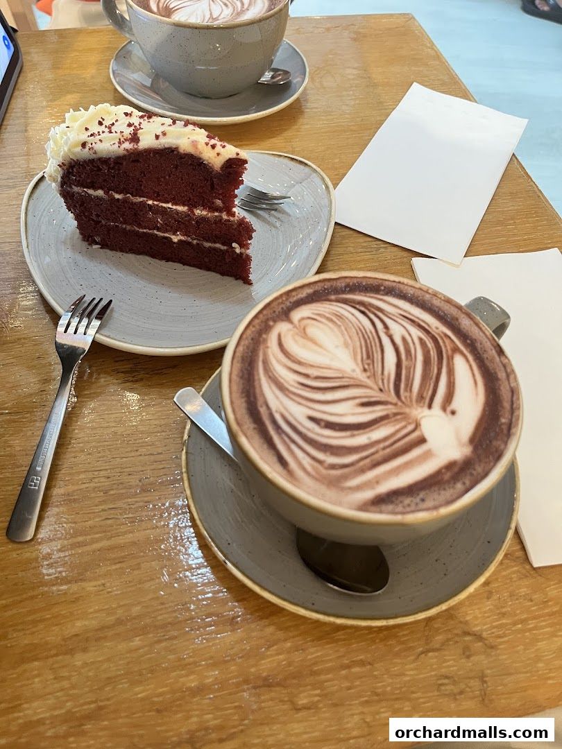 A slice of red velvet cake and two cups of hot chocolate on a wooden table.