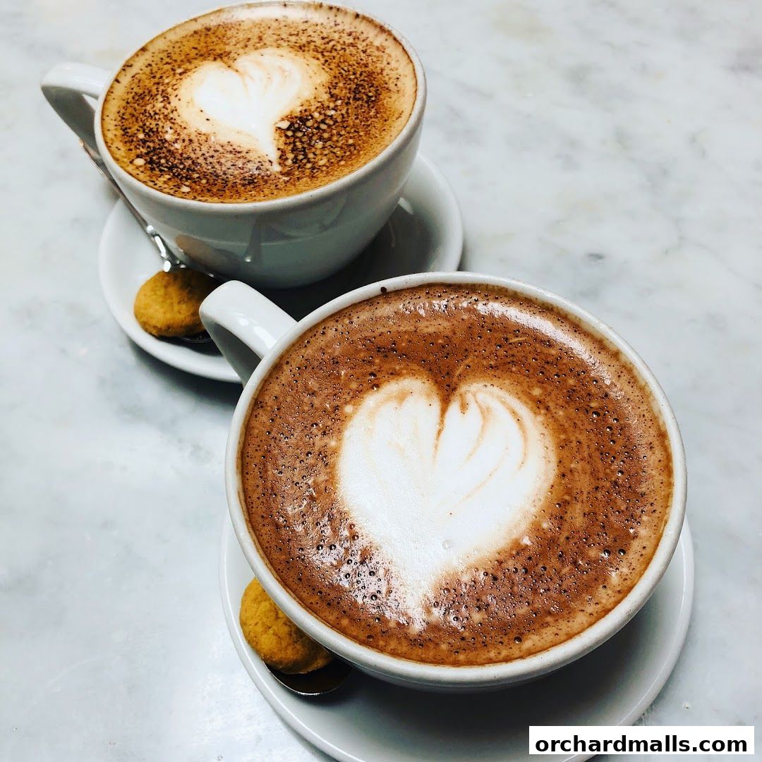 Two cups of coffee with heart-shaped latte art and cookies on a marble surface.