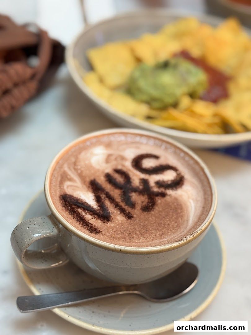 A cup of hot chocolate with 'MHS' dusted on top, next to a bowl of nachos.