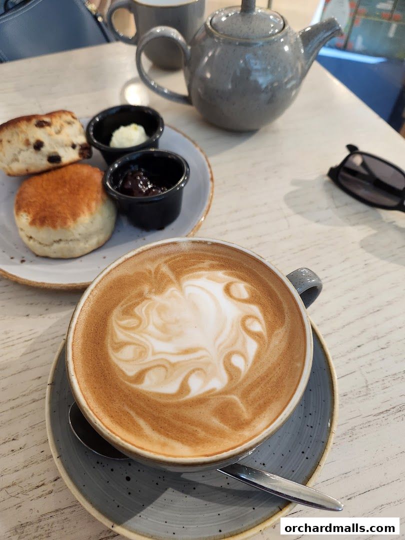A close-up of a latte with latte art, scones, jam, and butter.