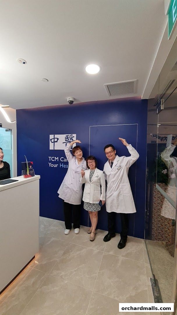 Three staff members in white coats pose in front of the Sin Kang TCM Clinic branding.