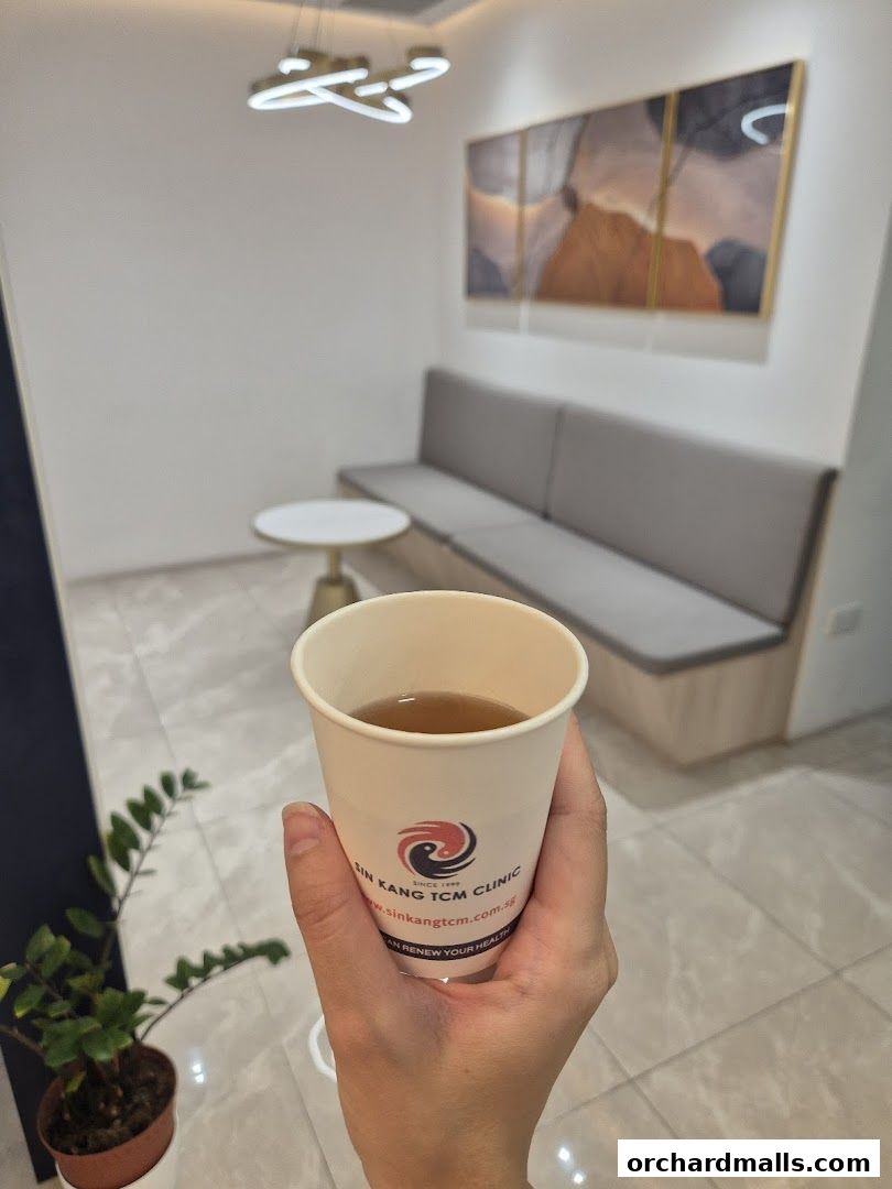 A hand holds a cup of herbal tea in a waiting area of a TCM clinic.