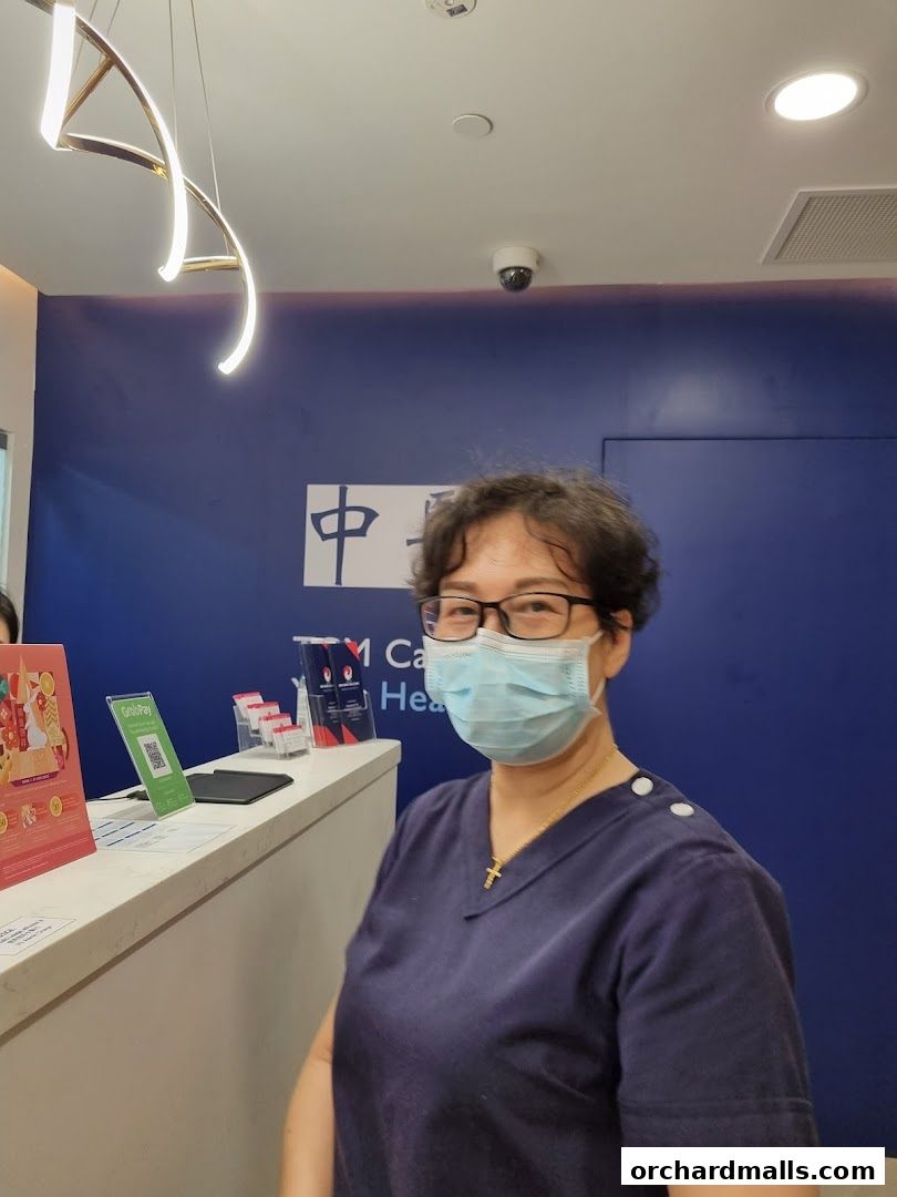 A staff member at Ma Kuang Holistic TCM Wheelock Place smiles behind a counter.