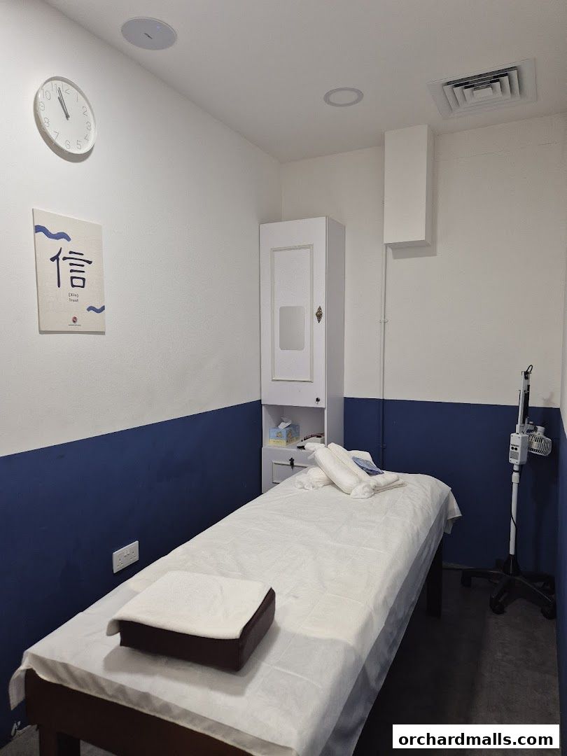 A treatment room with a massage bed, cabinet, and a clock on the wall.