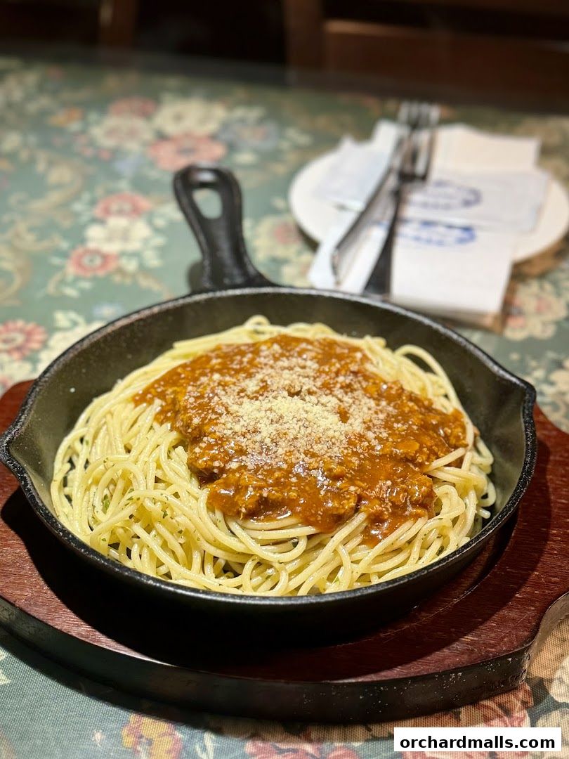 A close-up of spaghetti bolognese served in a cast-iron skillet on a floral tablecloth.