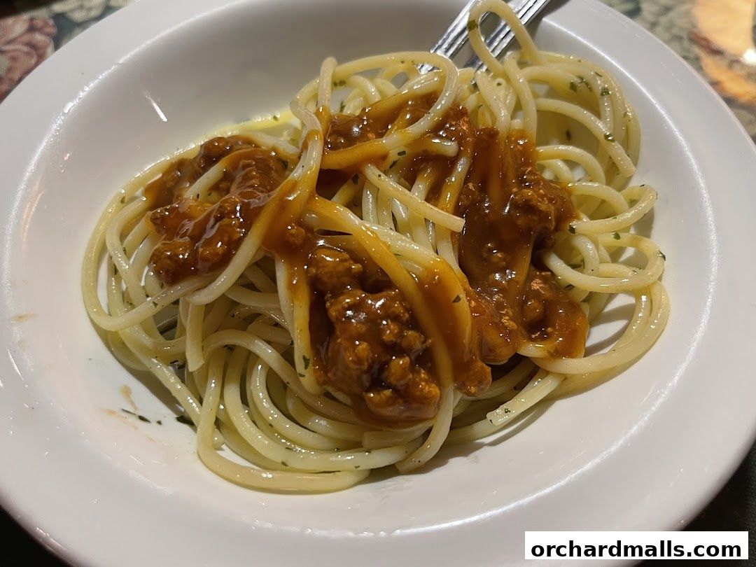 A close-up shot of spaghetti with a rich meat sauce in a white bowl.