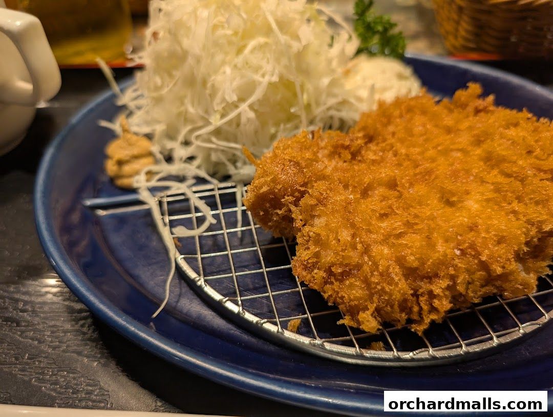 A close-up of a crispy fried cutlet served with shredded cabbage and a dollop of mustard.