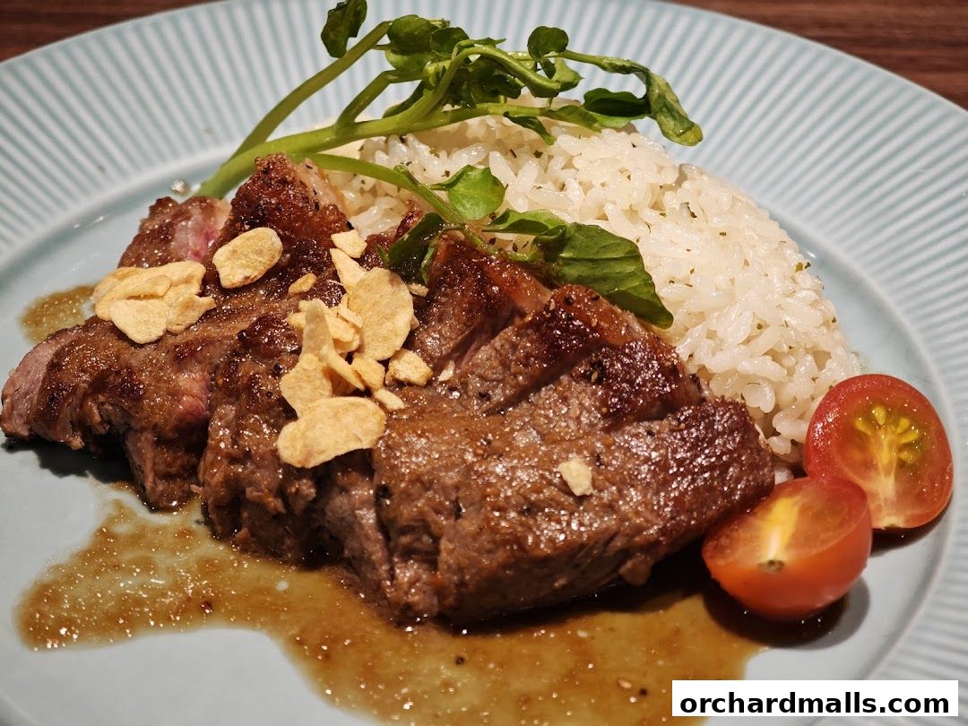 A plate of sliced steak with rice, garnished with crispy garlic and cherry tomatoes.