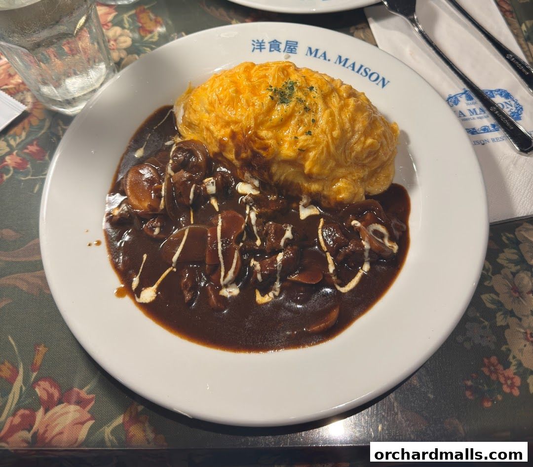 A plate of omurice with beef stew and a glass of water on a floral tablecloth.
