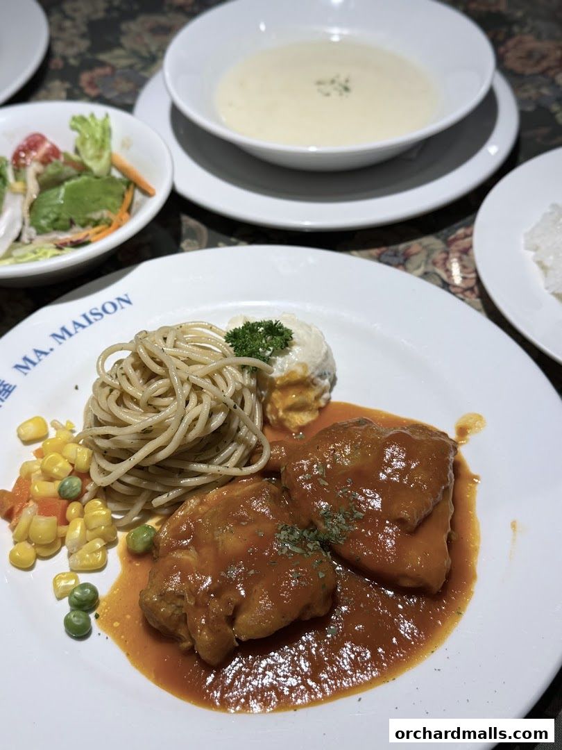 A plate of spaghetti with chicken in tomato sauce, served with a side salad and soup.