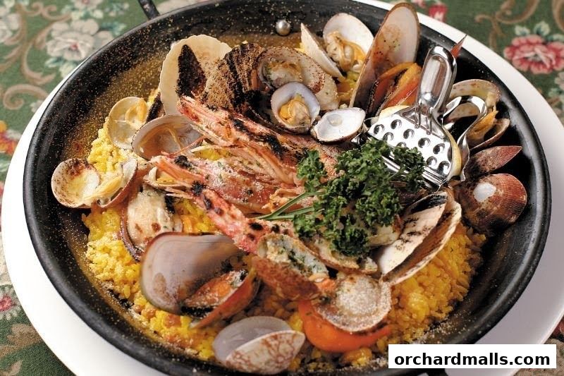 A close-up of a seafood paella dish with prawns, clams, and mussels in a black pan.