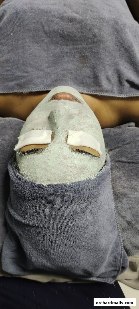 A person's face covered in a green mask with white eye pads, wrapped in towels.